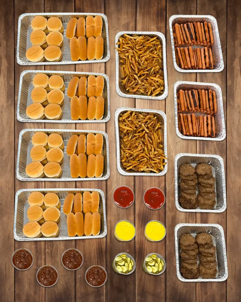 Large catering bar with buns, fries, burger patties, hot dogs, and condiments.
