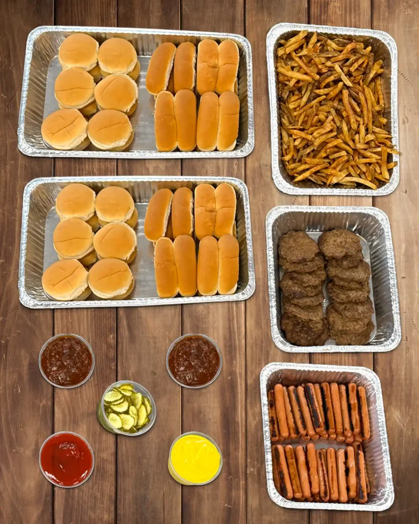 Medium catering bar with buns, fries, burger patties, hot dogs, and condiments.